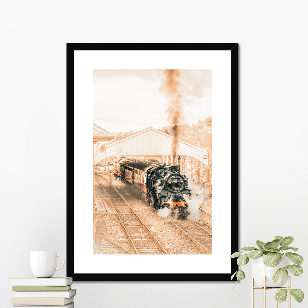 Framed photograph of a steam train on tracks with a white wall background