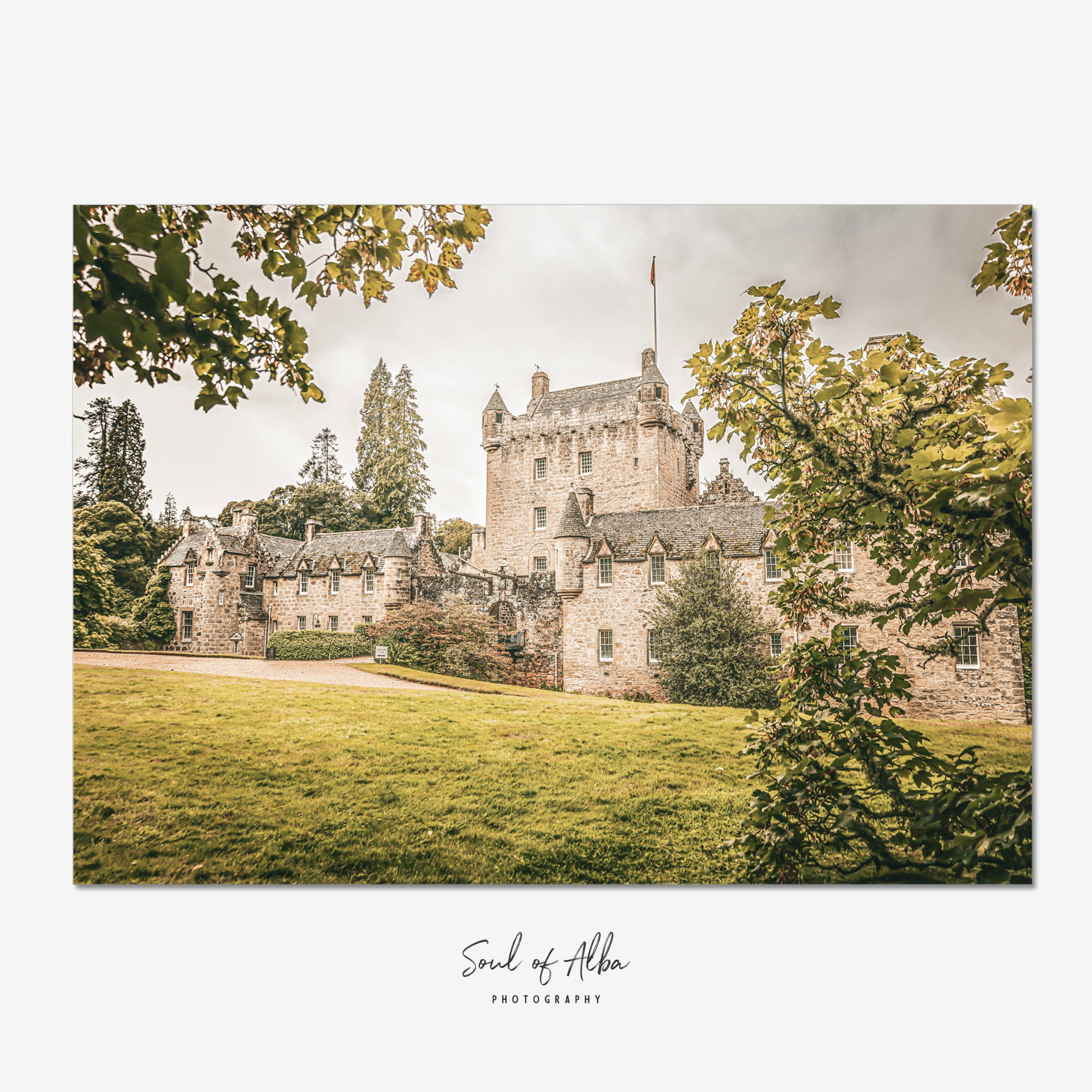 Fine art photograph of Cawdor Castle in the Scottish Highlands, framed by leafy trees and featuring its historic stone tower and courtyard.
