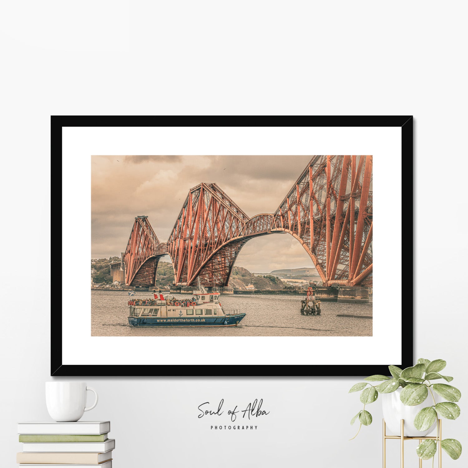 The iconic red Forth Bridge spanning the Framed Print of the Firth of Forth in Scotland with a passenger boat passing beneath its steel cantilever structure.