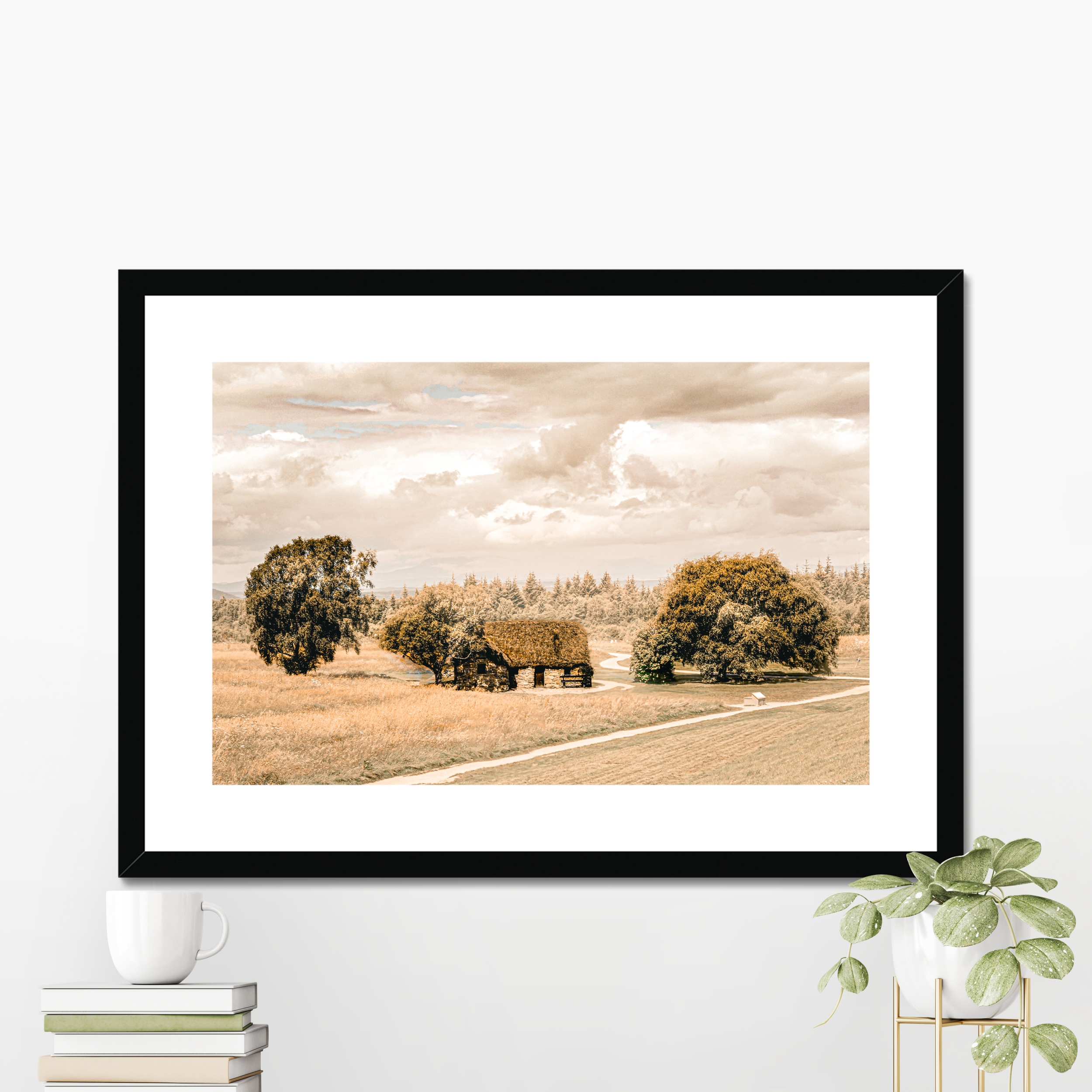 Framed landscape print of a field with trees and a road, displayed on a wall with a white background.