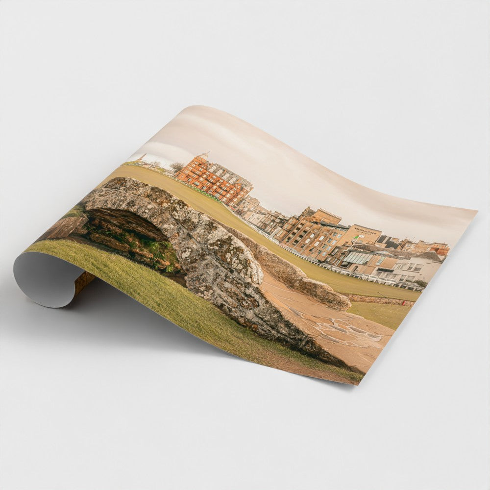 A close-up, angled view of a high-quality physical paper print of the St Andrews golf course being unrolled, showcasing the matte texture and detail of the Scottish heritage photography.