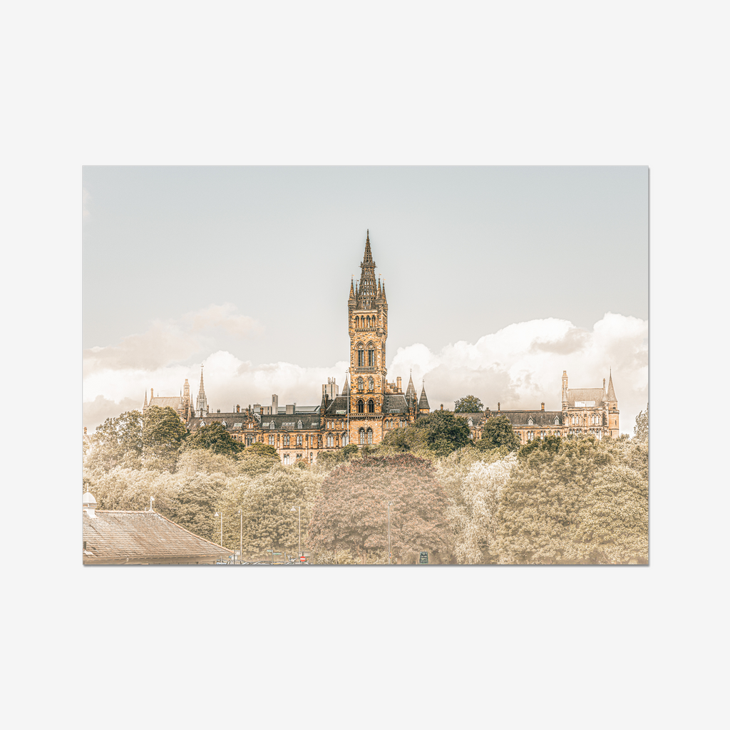 Fine art landscape photograph of the University of Glasgow’s Gothic spire rising above the treetops of the West End. The historic sandstone architecture is captured in warm, sun-drenched tones under a bright, cloud-filled sky.