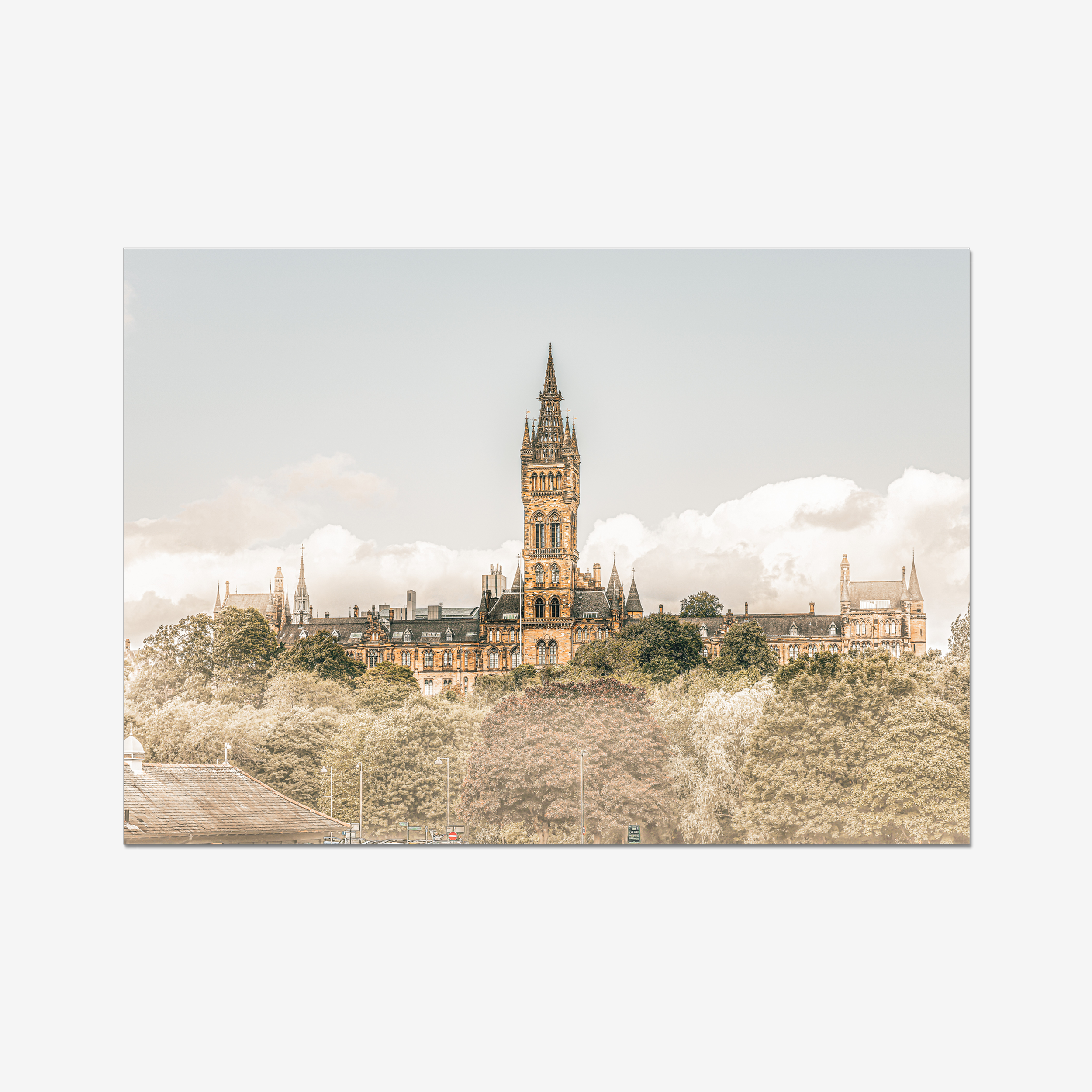 Fine art landscape photograph of the University of Glasgow’s Gothic spire rising above the treetops of the West End. The historic sandstone architecture is captured in warm, sun-drenched tones under a bright, cloud-filled sky.