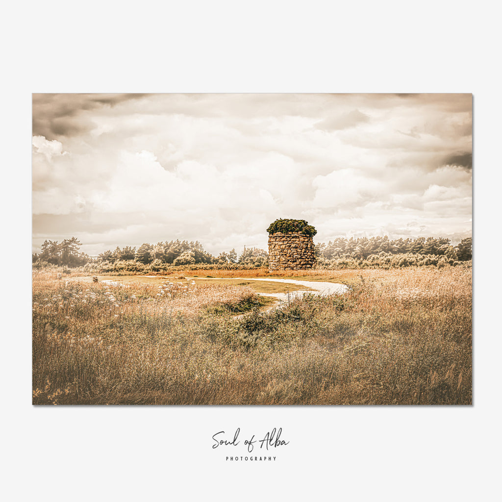Memorial cairn standing on Culloden Battlefield near Inverness, Scotland, beneath dramatic clouds and golden light.