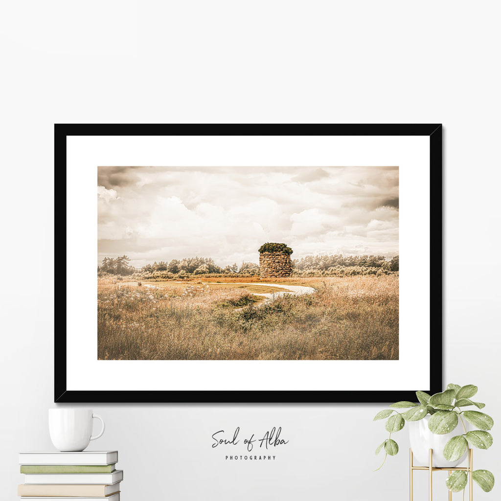Framed print of Memorial cairn standing on Culloden Battlefield near Inverness, Scotland, beneath dramatic clouds and golden light.
