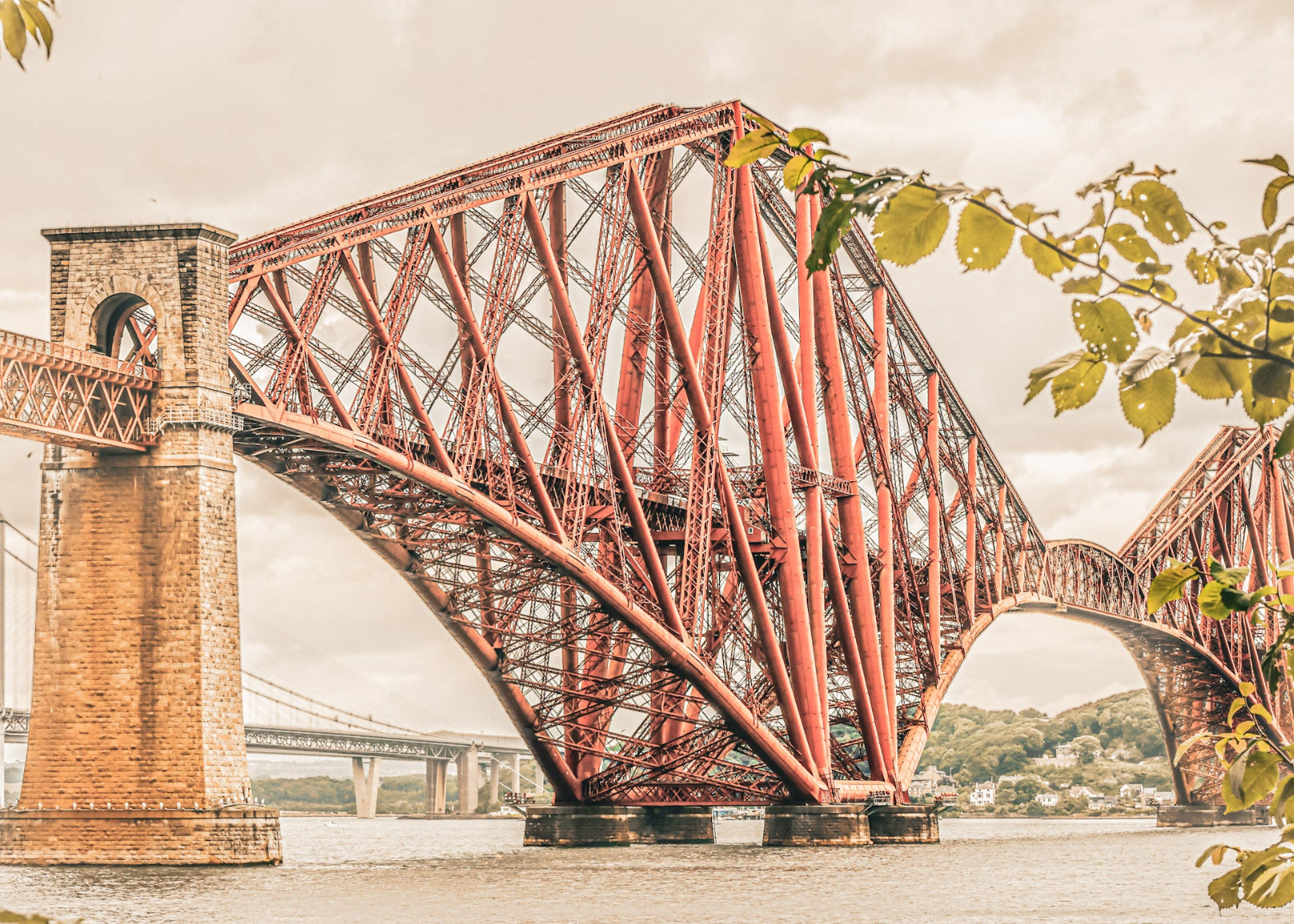 Red steel bridge over a body of water with leaves framing the edges.